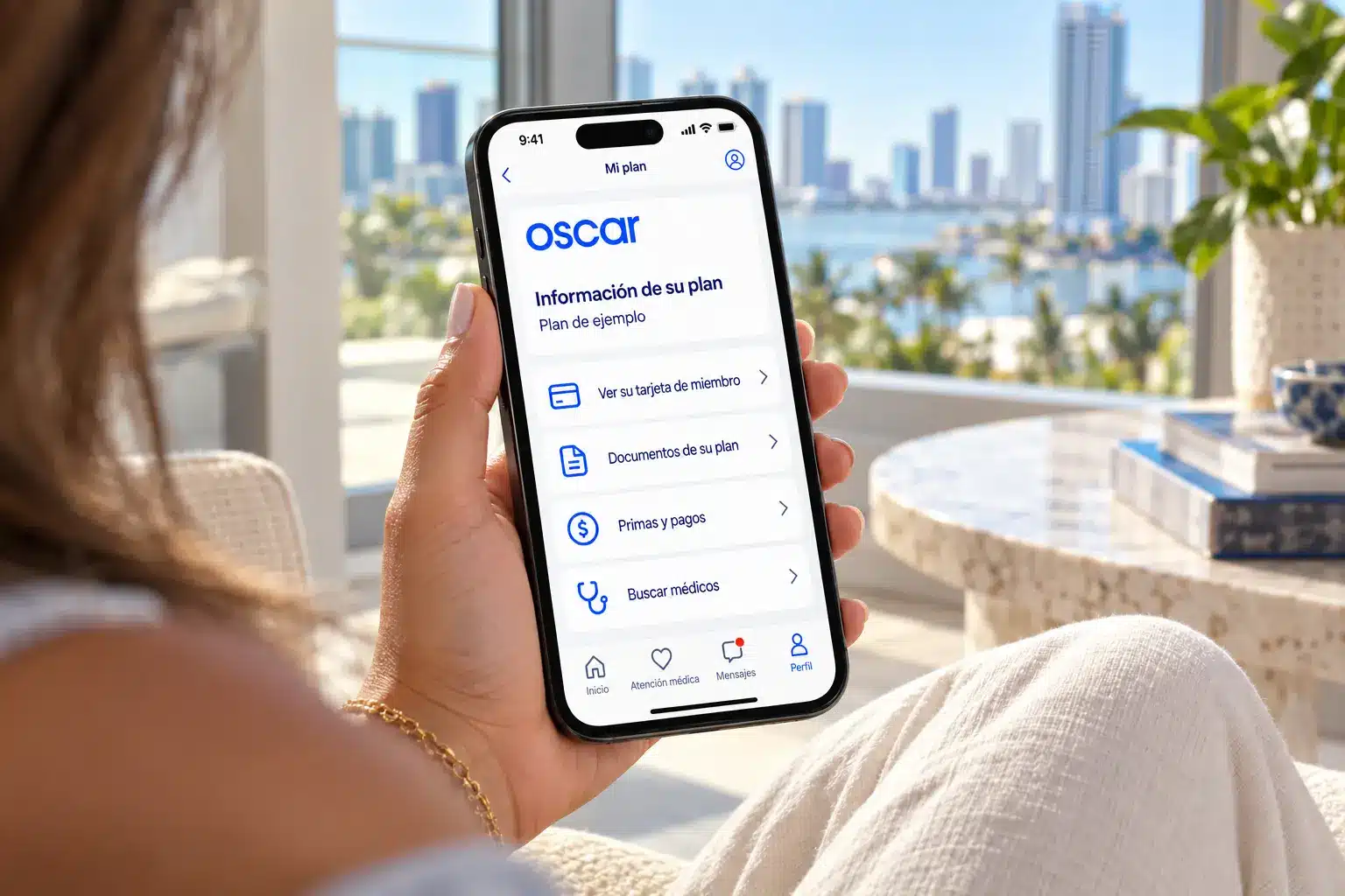 Oscar en Florida | TuSeguroMédicocom Mujer sostiene un teléfono con una vista ilustrativa de la aplicación de Oscar en español junto a una ventana con vistas a Miami